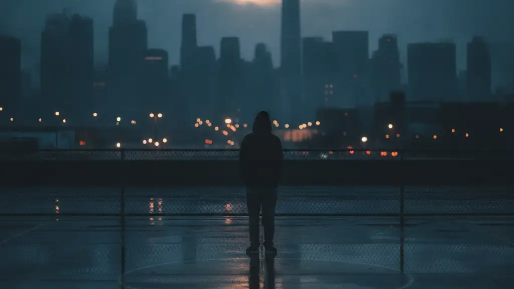 Silhouetted young person on empty basketball court, looking at city skyline.