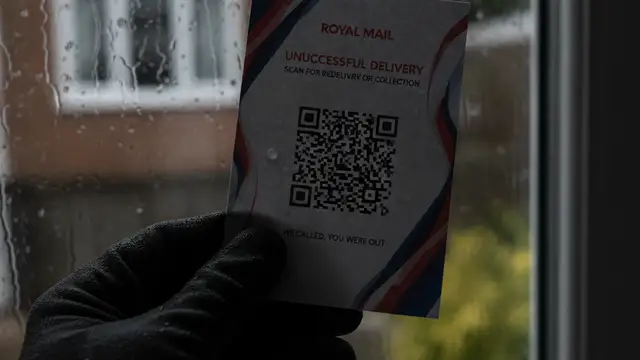 Close-up of a Royal Mail delivery card with a QR code, held by a gloved hand.