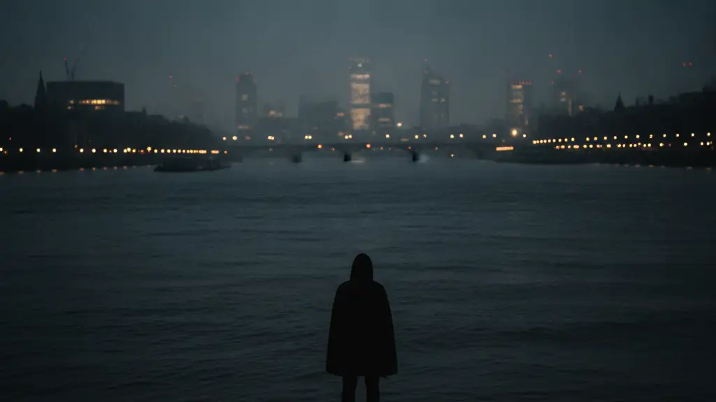 Silhouetted figure on Thames bank at dusk, looking at dark water.