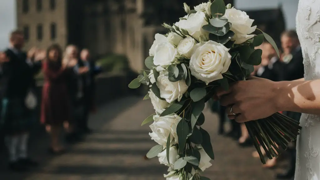 Bride's hand with wedding ring holding a white rose bouquet.