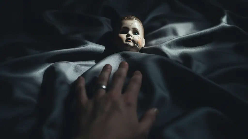 A porcelain doll on dark silk, a blurred hand with a ring reaching towards it.