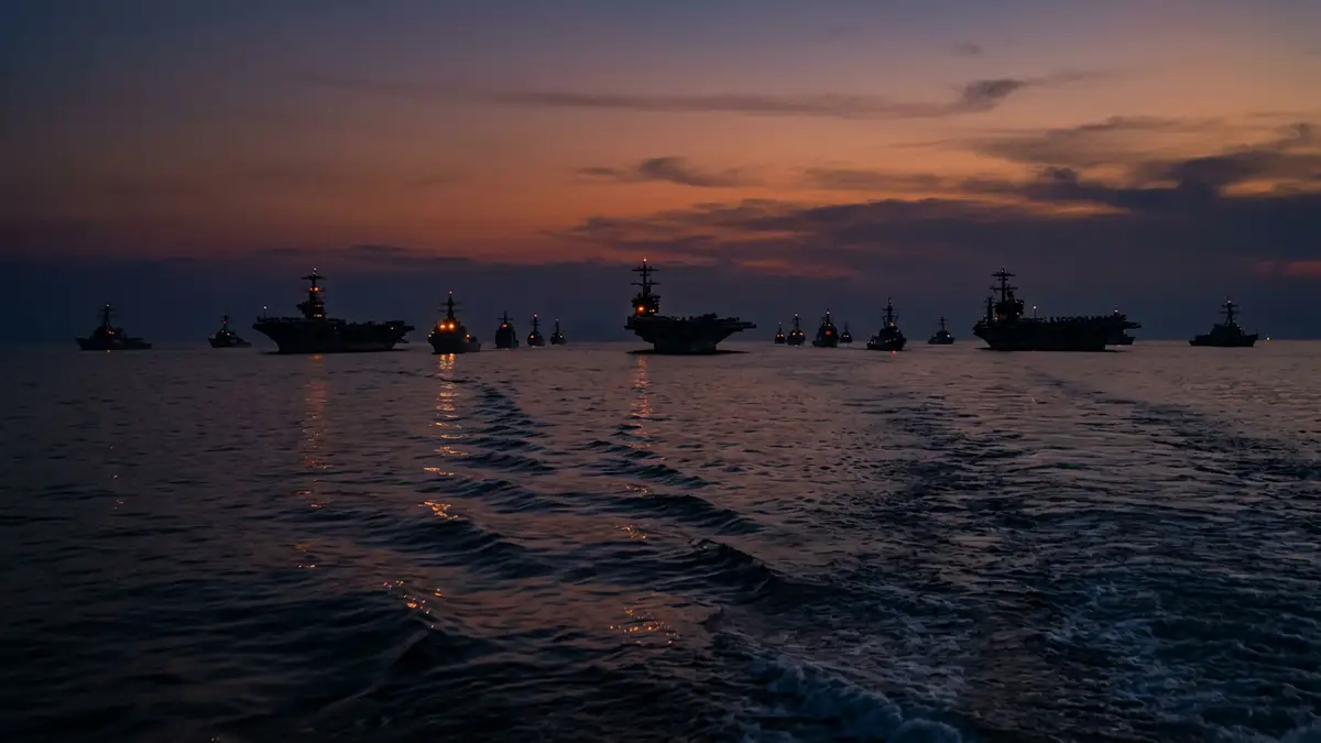 Silhouettes of naval warships on a dark ocean at sunset under a dramatic sky.