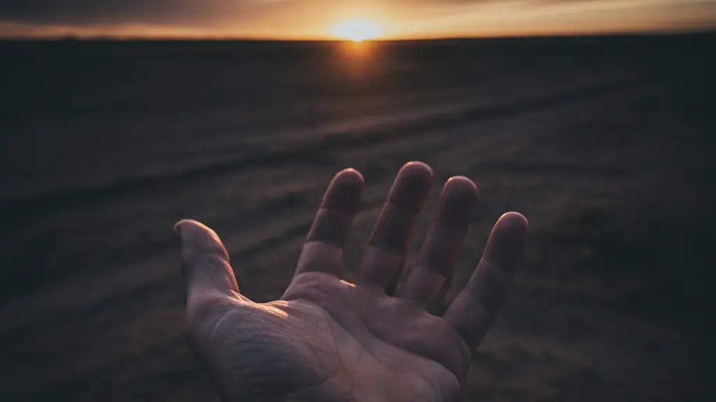 A weathered hand reaching towards a distant, setting sun over an empty landscape.