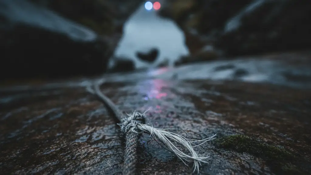 A frayed climbing rope on a dark, wet rock face with distant emergency lights.