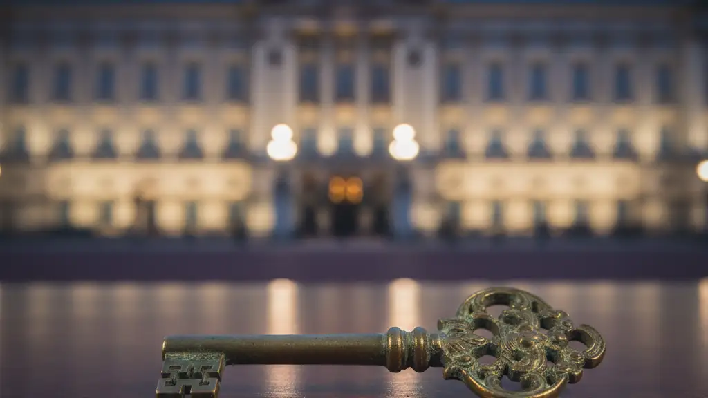 An antique brass key resting on dark wood, with Buckingham Palace blurred in the background.