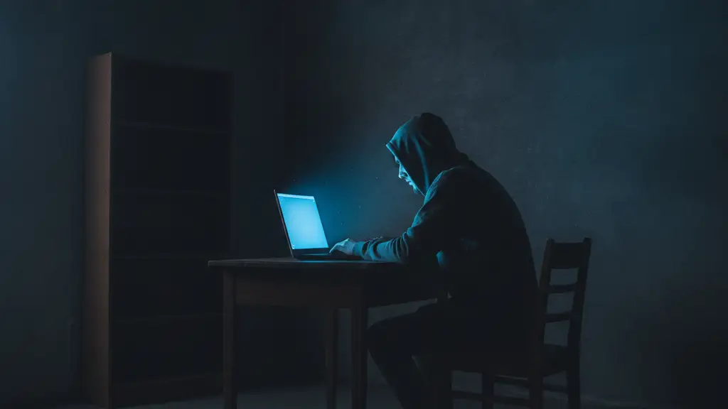 Silhouette of a person hunched over a glowing laptop in a dark room.