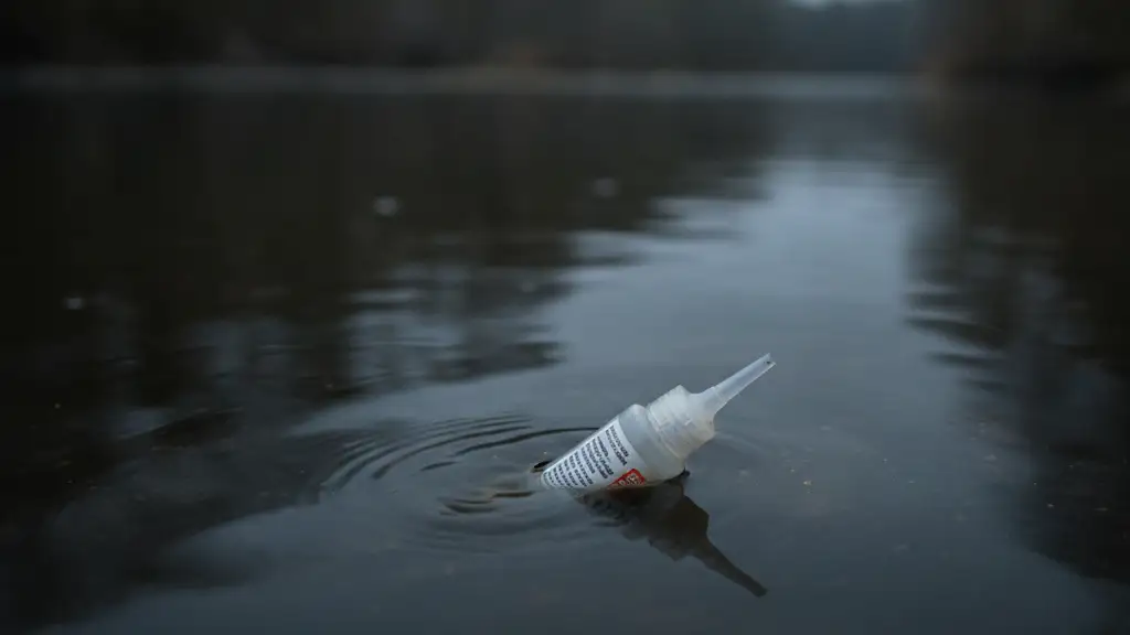 Discarded pet flea treatment applicator partially submerged in murky river water.