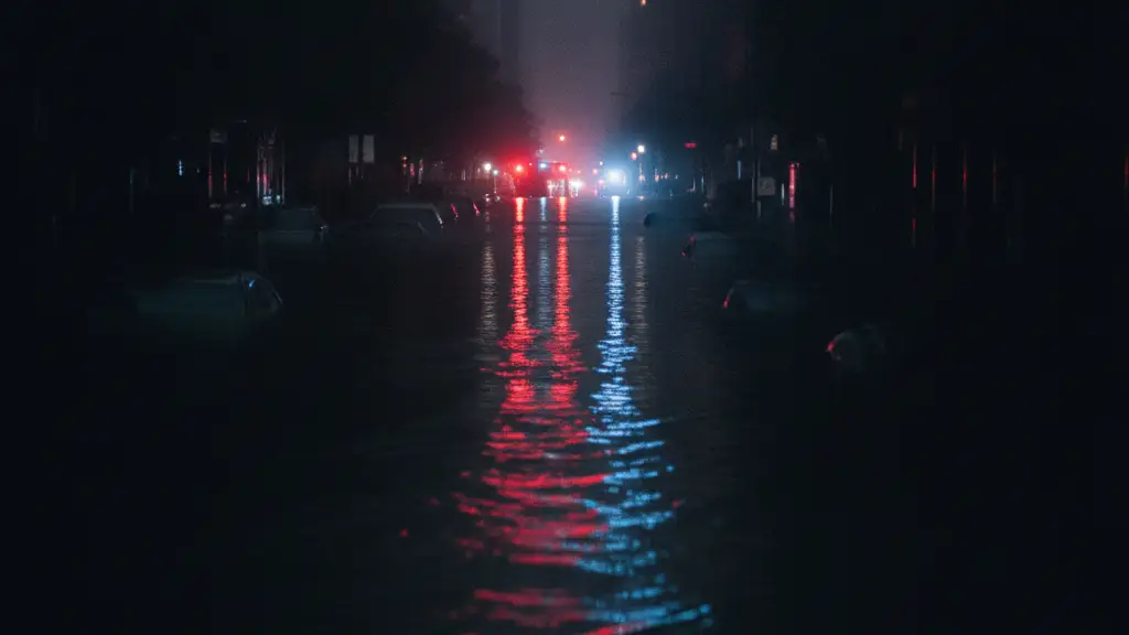 Emergency lights reflecting in deep floodwaters on a dark, rain-soaked street.