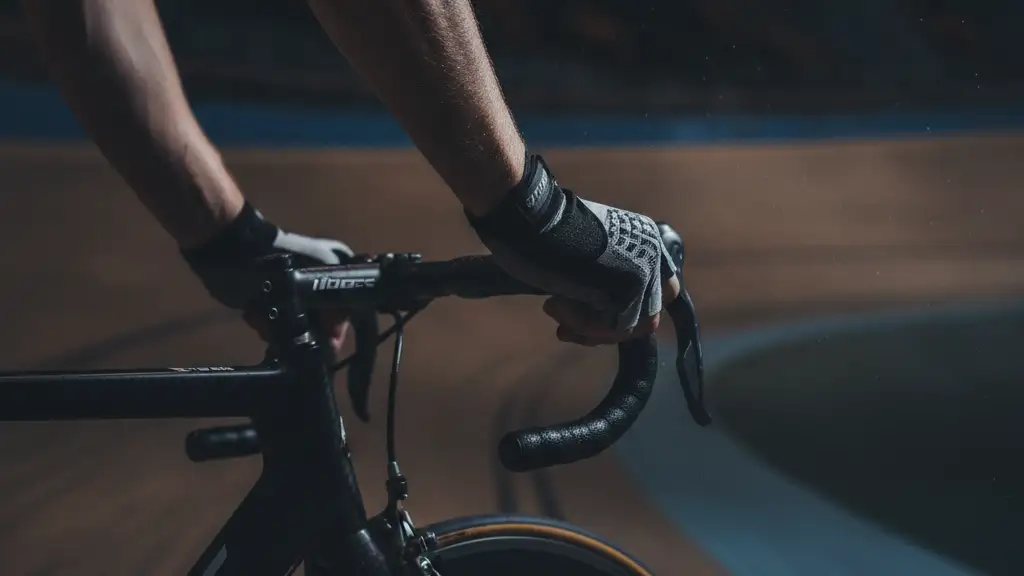 Cyclist's gloved hand gripping handlebars on a dark velodrome track.