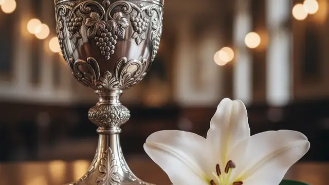 A silver chalice and a white lily on a dark wooden table in soft light.