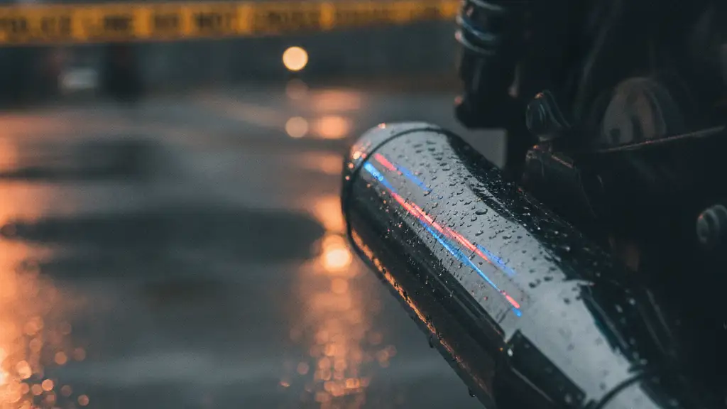 Motorcycle exhaust reflecting emergency lights on wet asphalt, with blurred police tape.