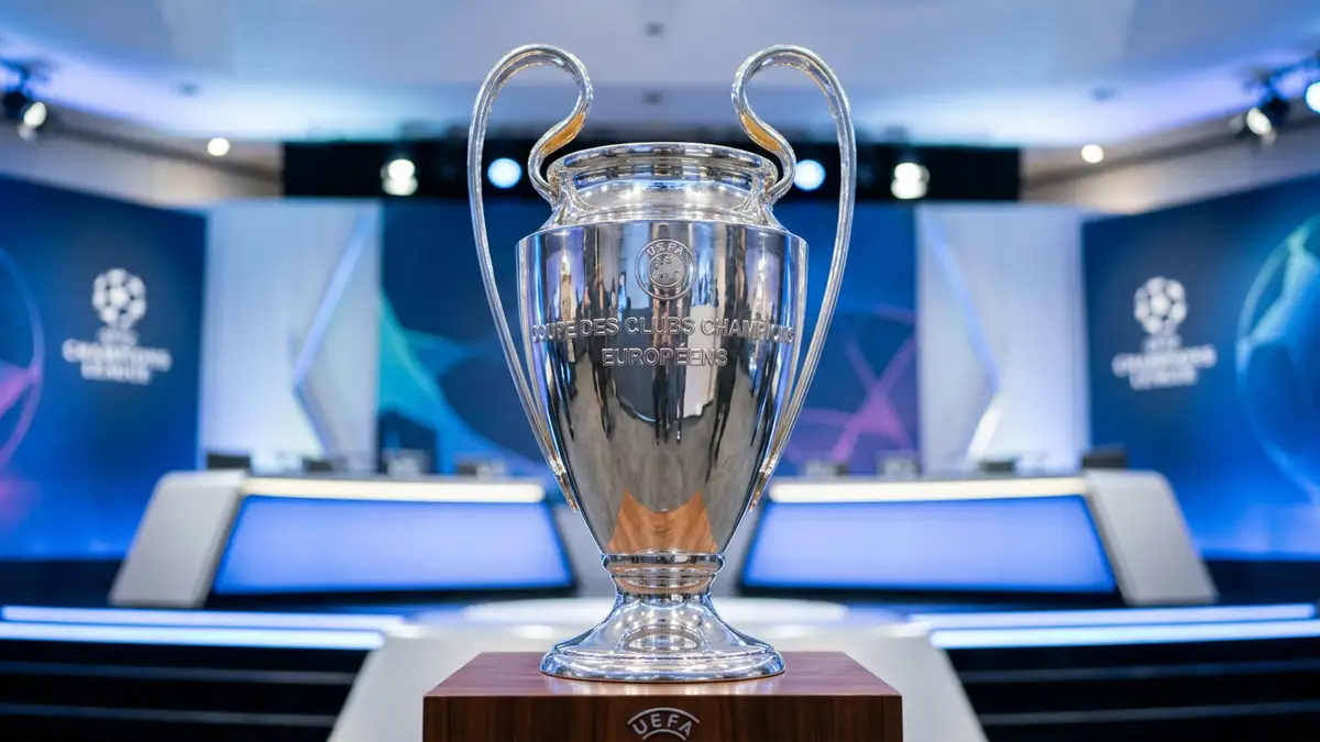The silver Champions League trophy stands on a pedestal under bright studio lights.
