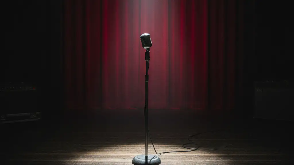 A lone microphone stand under a single spotlight on a dark stage.
