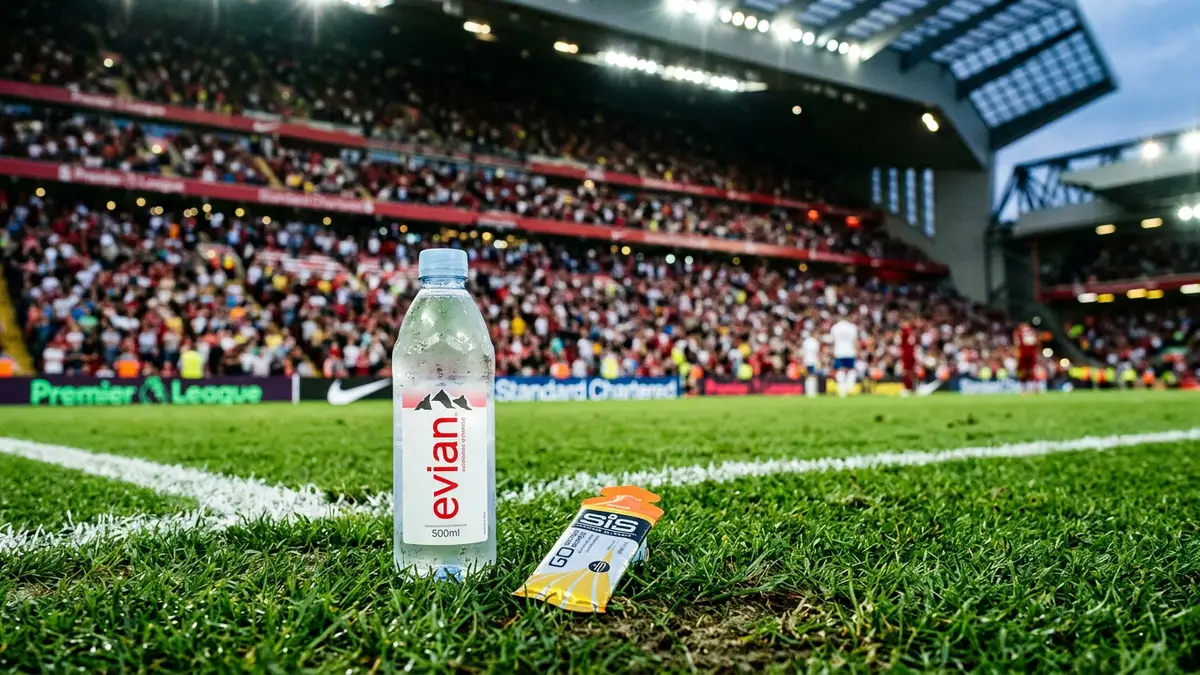 A water bottle and energy gel sit on a football pitch under stadium lights.