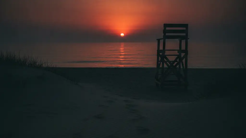 Empty lifeguard chair on a beach at sunset, footprints in sand.