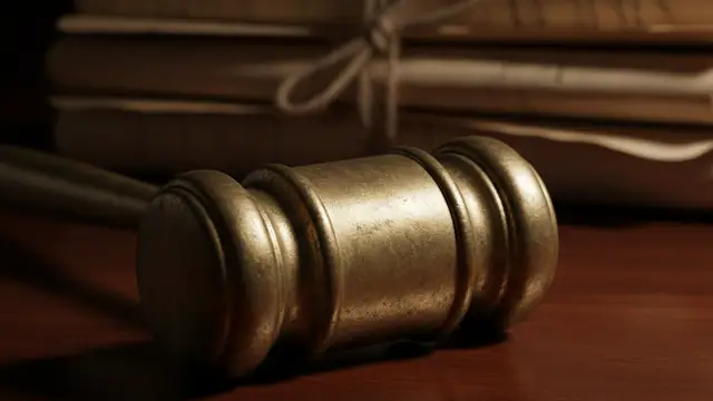 A brass gavel rests on a dark wooden surface next to old legal documents.
