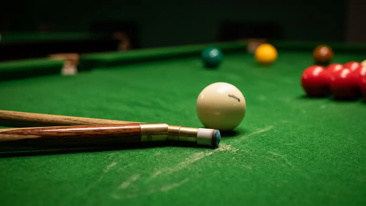 Snooker cue resting on green table felt, cue ball and colored balls in soft focus.