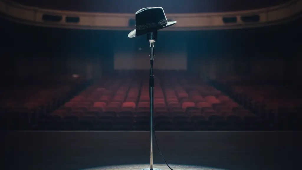 A fedora on an empty microphone stand on a dimly lit stage.