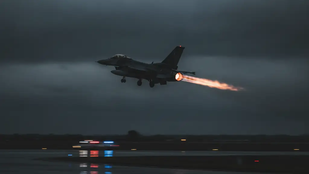 Silhouette of a fighter jet taking off at twilight, emergency lights reflecting below.