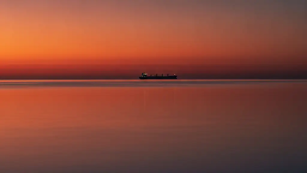 Distant cargo ship silhouette on calm ocean at dusk, reflecting dramatic sky.