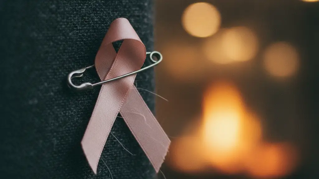 A pink awareness ribbon pinned to dark fabric, with soft, blurred background.