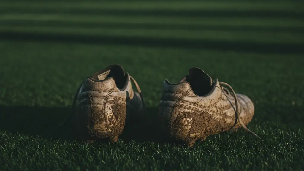 Worn football boots on a green pitch, blurred figures in background.