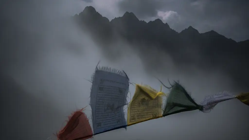 A tattered prayer flag flutters in strong wind and mist against a blurred mountain silhouette.