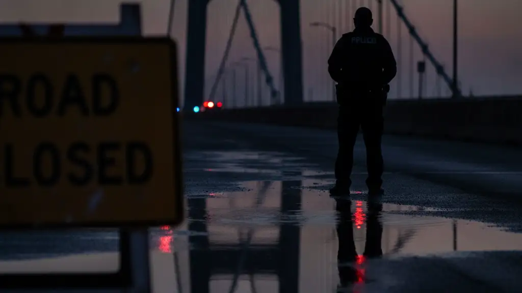 Traffic officer silhouette against a suspension bridge with emergency lights reflecting in a puddle.