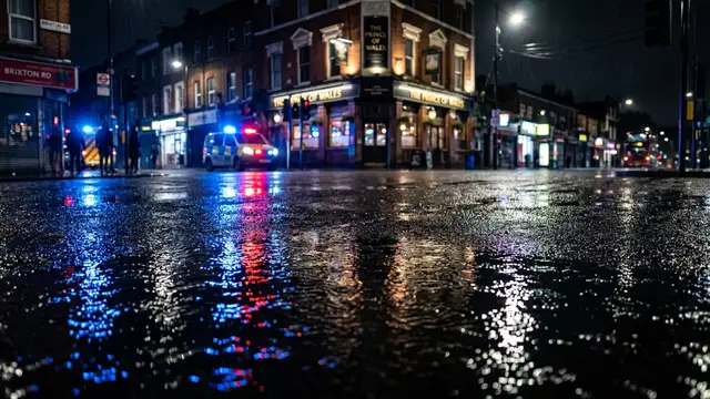 Emergency lights reflecting on wet pavement at night in a city.