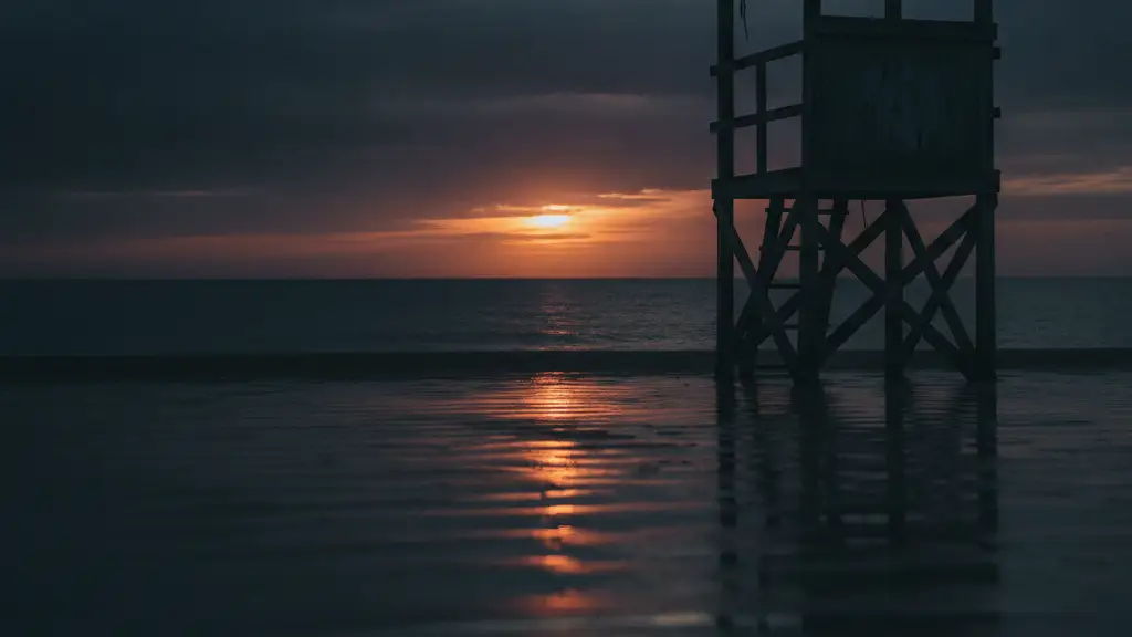 Lifeguard stand silhouette against a dramatic, overcast sunset over a dark ocean.