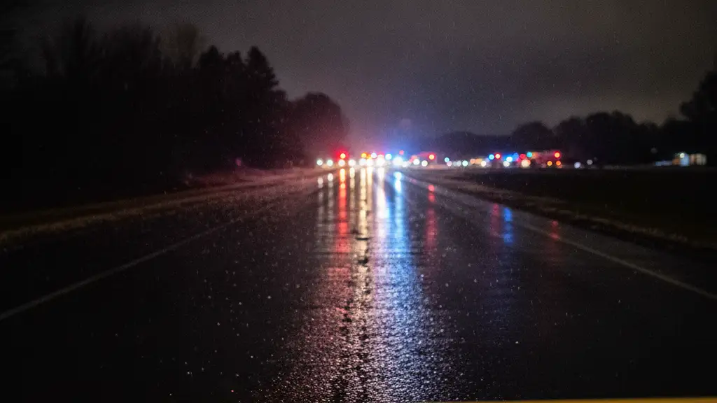 Police tape in foreground, reflecting emergency lights on wet road at night.