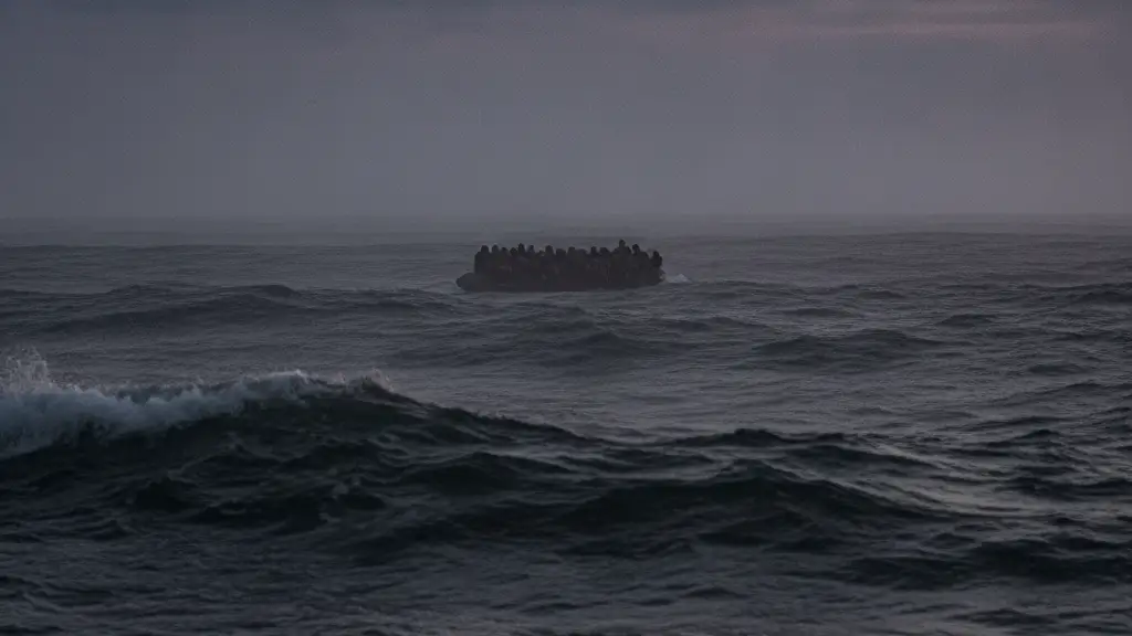 A small, overcrowded dinghy, silhouetted against a stormy sea at dusk, shrouded in mist.