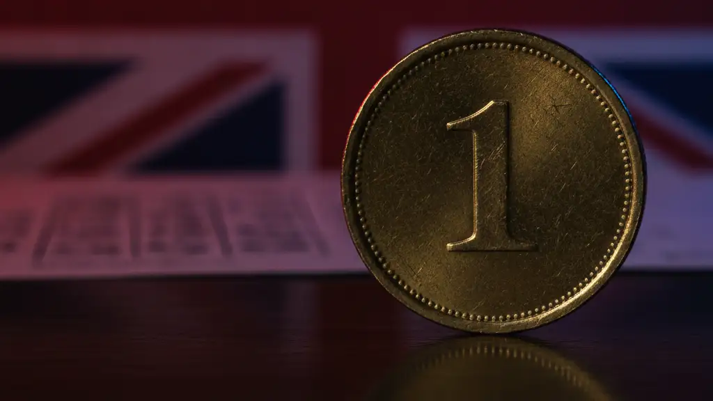 A single gold coin reflecting British flag colors, resting on a dark surface.
