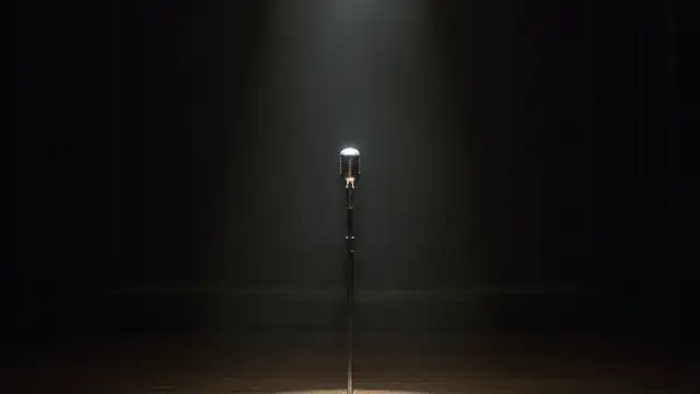 Empty concert stage with a single microphone stand under a spotlight.