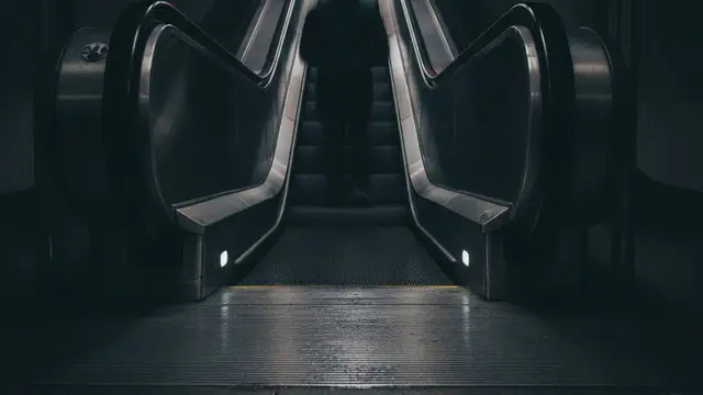 Blurred figure on a London Underground escalator with emergency light reflections.