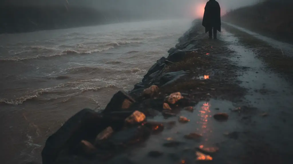 Silhouetted figure in heavy rain overlooking a turbulent, flooded river.