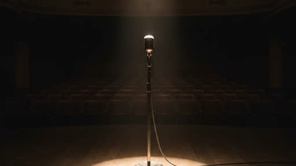 A lone vintage microphone stand on a dimly lit, empty stage.