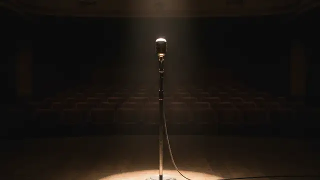 A lone vintage microphone stand on a dimly lit, empty stage.