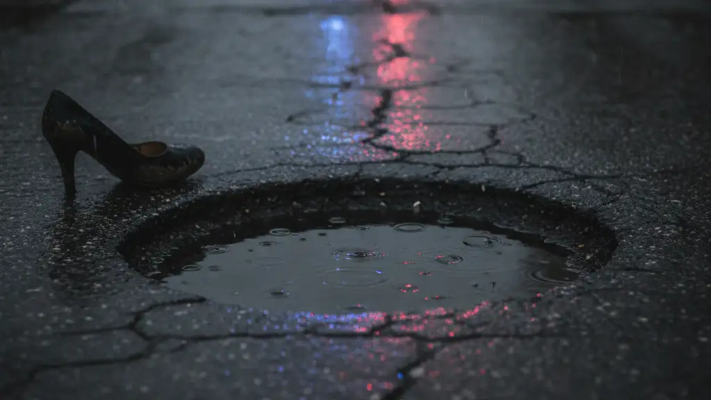 A single high-heeled shoe lies near a deep pothole on a wet, cracked road.