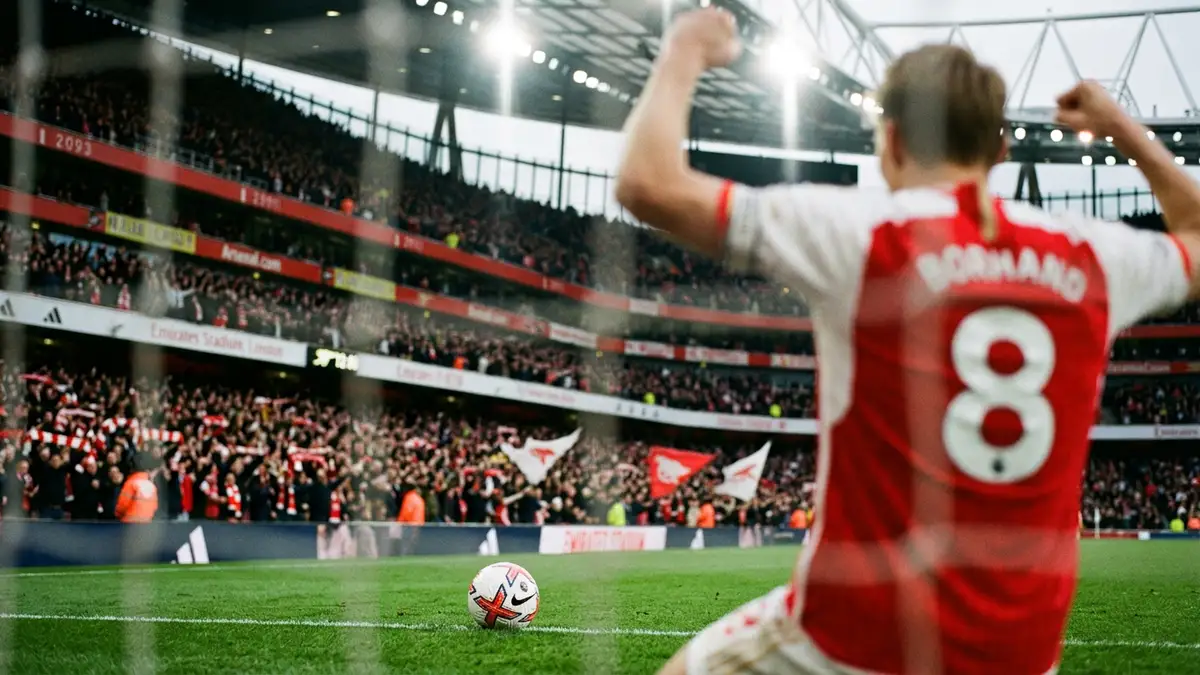 A blurred Arsenal player celebrates in front of a cheering stadium crowd from behind.