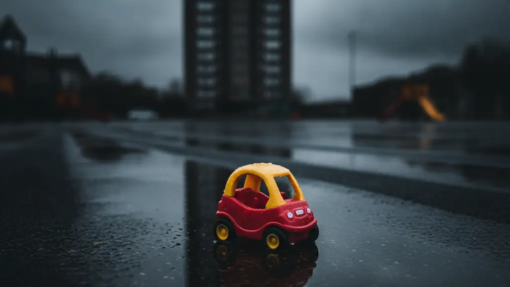 A small toy car on a wet playground, with a tall apartment building in the background.