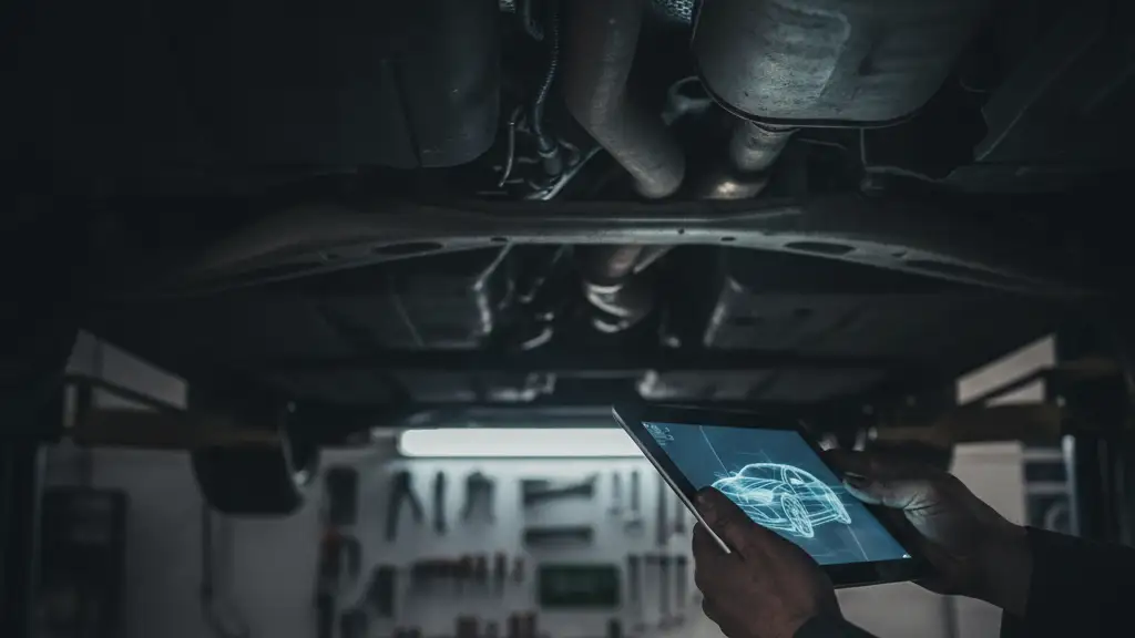 Mechanic's hand with tablet under car, glowing screen, dark garage.