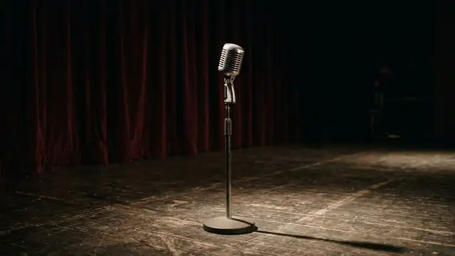Vintage microphone on an empty, dimly lit stage, illuminated by a single spotlight.