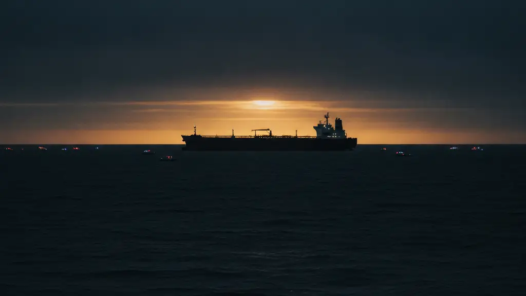 Silhouetted oil tanker at dusk, distant emergency lights reflecting on water.