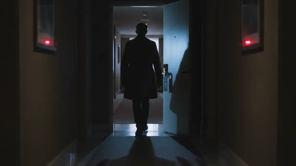 Blurred figure in a dimly lit hotel hallway, walking away from an ajar door.