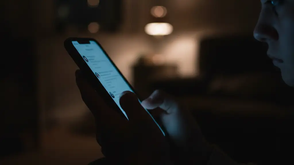 Silhouetted teenage hand holding a glowing smartphone in a dark room.