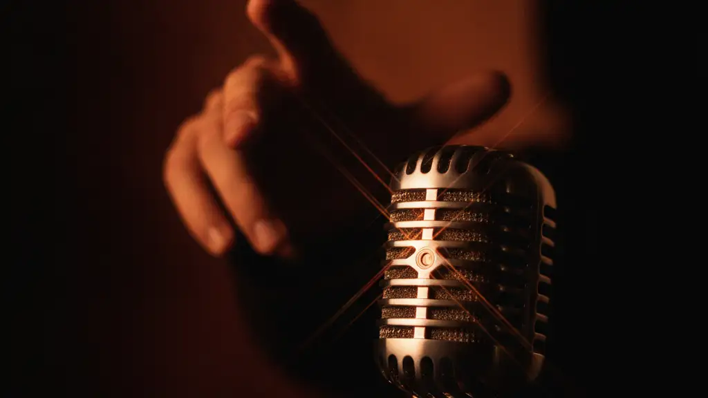 A vintage microphone reflecting light, with a blurred hand silhouette in the background.