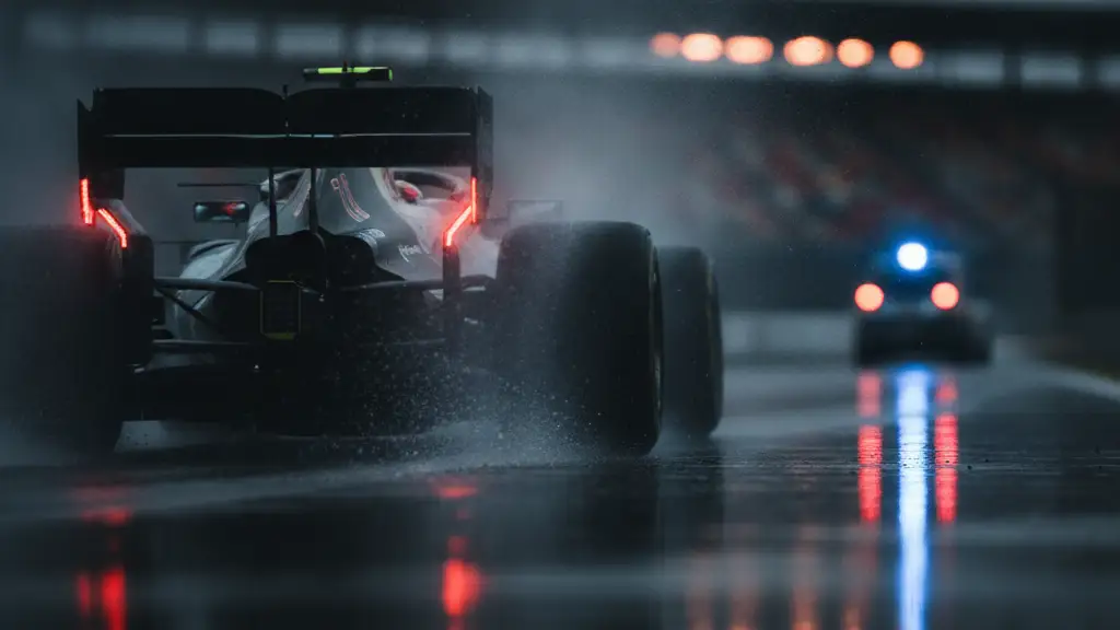 Rear view of a blurred Formula 1 car on a wet track, spray rising.