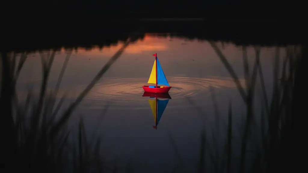 A small toy boat floats alone on a dark, still pond at sunset.