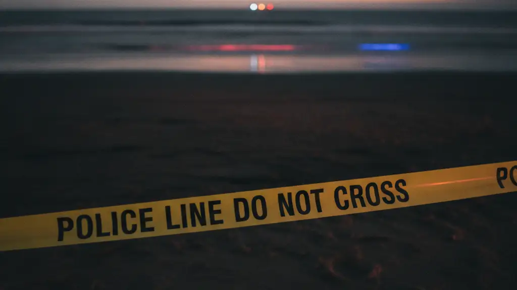 Police tape on a dark, wet beach with distant emergency light reflections at dawn.